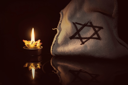A burning candle next to the star of David on a black background. A symbol of remembrance of the victims of the genocide of the Jew in the third Reich in Germany.